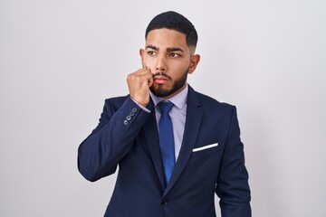 Young hispanic man wearing business suit and tie looking stressed and nervous with hands on mouth biting nails. anxiety problem.