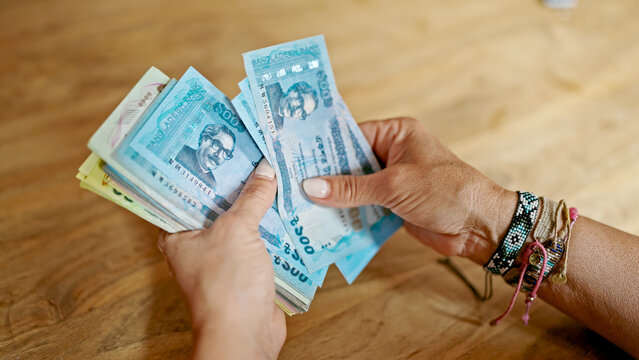 Middle age hispanic woman counting bangladesh taka banknotes at home