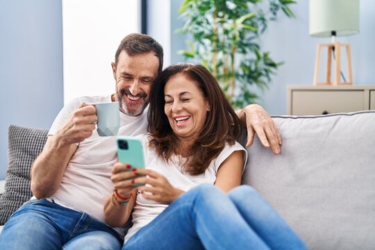 Middle age man and woman couple using smartphone and drinking coffee at home