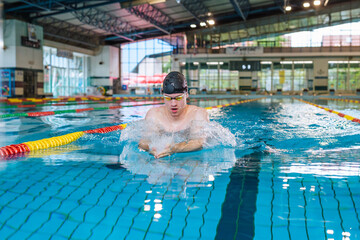 Male athlete swimming in breaststroke style in the pool, stroke, immerse, and lift out of the water...