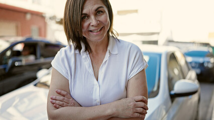 Middle age hispanic woman smiling confident with crossed arms in front of the car at street
