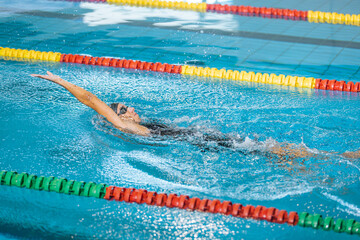 Professional female athlete swimming backstroke in the pool, arms movement. Competitive swimming drills concept.
