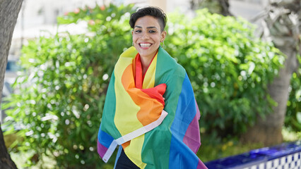Young beautiful hispanic woman smiling confident wearing rainbow flag at park
