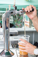 Man pouring beer in a plastic glass at a street stall. Summer festivals.