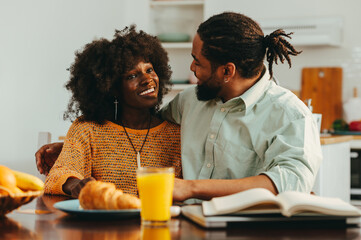 Fototapeta na wymiar An african american husband and wife are hugging and bonding while sitting at the breakfast table at home.