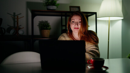 Young redhead woman using laptop sitting on table at home
