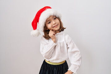 Little hispanic girl wearing christmas hat smiling looking confident at the camera with crossed arms and hand on chin. thinking positive.