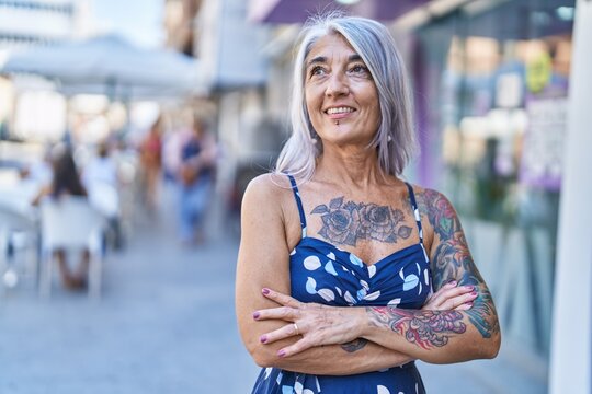 Middle age grey-haired woman standing with arms crossed gesture at street