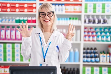 Young caucasian woman working at pharmacy drugstore showing and pointing up with fingers number eight while smiling confident and happy.