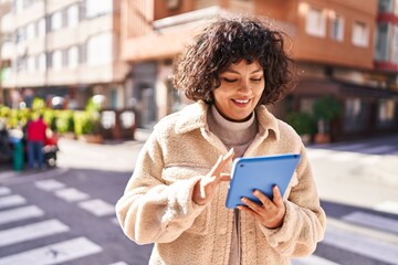 Young beautiful hispanic woman smiling confident using touchpad at street