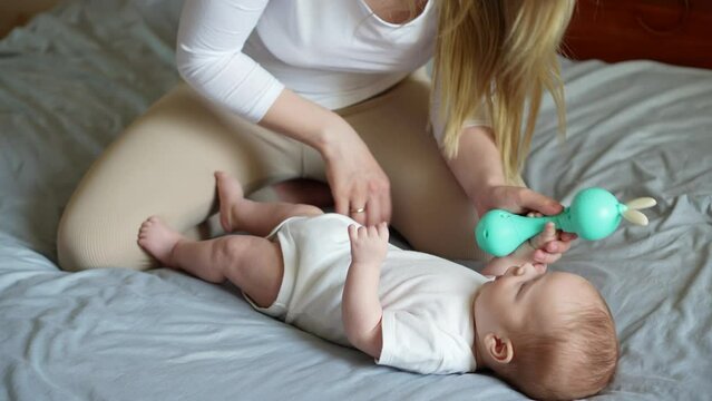 A happy mom tickles a charming baby, plays with a rattle,developing motor skills,visual, auditory skills.Children's Day.