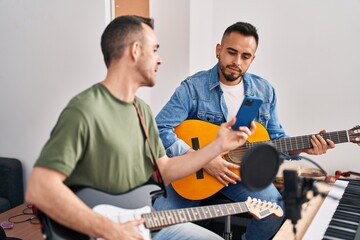 Two men musicians playing classical and electrical guitar looking smartphone screen at music studio