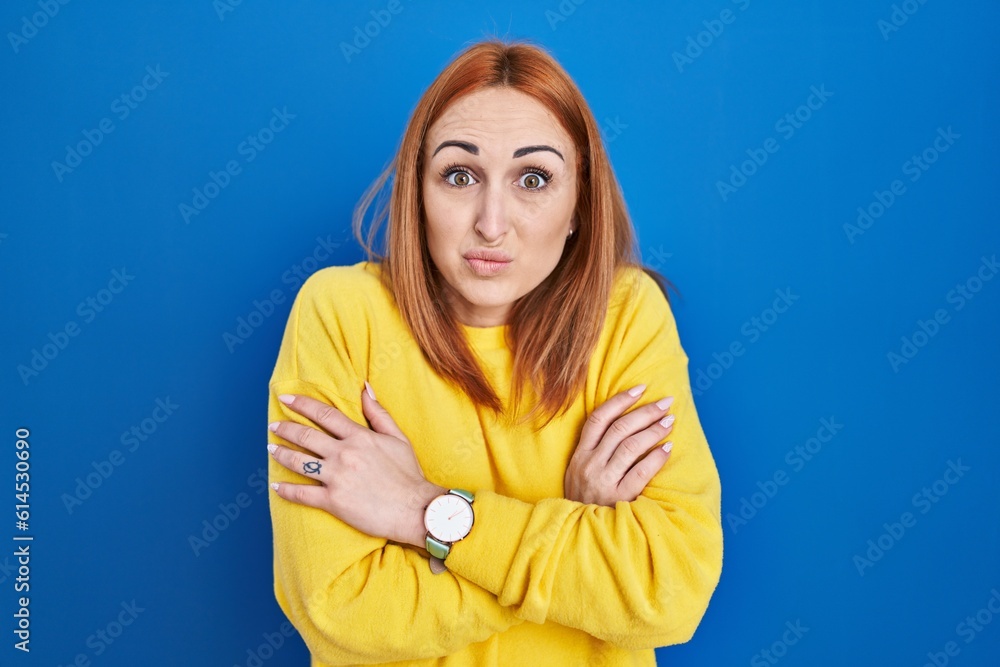 Sticker young woman standing over blue background shaking and freezing for winter cold with sad and shock ex