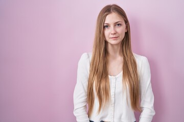 Young caucasian woman standing over pink background relaxed with serious expression on face. simple and natural looking at the camera.