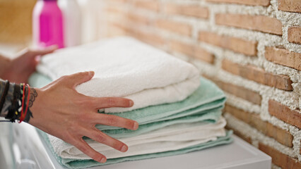 Young hispanic man touching folded towels at laundry room