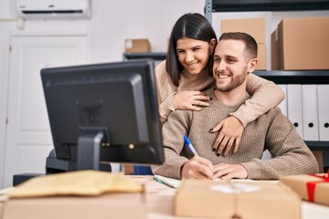 Man and woman ecommerce business workers hugging each other write on notebook at office