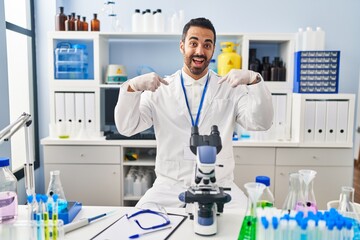 Young hispanic man with beard working at scientist laboratory looking confident with smile on face,...