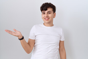 Young non binary man wearing casual white t shirt smiling cheerful presenting and pointing with palm of hand looking at the camera.