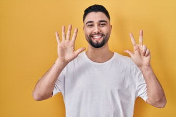 Young handsome man wearing casual t shirt over yellow background showing and pointing up with fingers number eight while smiling confident and happy.