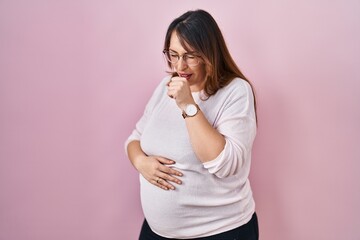 Pregnant woman standing over pink background feeling unwell and coughing as symptom for cold or...