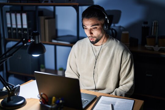 Young handsome man working using computer laptop at night afraid and shocked with surprise expression, fear and excited face.