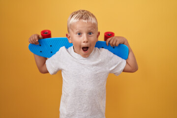 Little caucasian boy holding skate afraid and shocked with surprise and amazed expression, fear and...