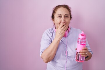 Senior woman wearing sportswear and headphones laughing and embarrassed giggle covering mouth with...