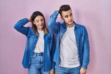 Young hispanic couple standing over pink background confuse and wondering about question. uncertain with doubt, thinking with hand on head. pensive concept.