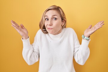 Young caucasian woman wearing white sweater over yellow background clueless and confused expression...