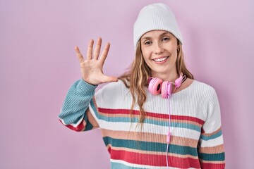 Obraz na płótnie Canvas Young blonde woman standing over pink background showing and pointing up with fingers number five while smiling confident and happy.