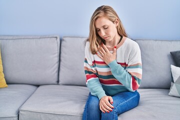 Young blonde woman sitting on sofa suffering heart attack at home
