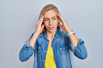 Young blonde woman standing over blue background with hand on head, headache because stress. suffering migraine.