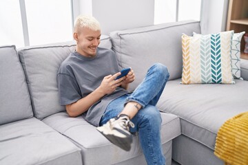 Young caucasian man using smartphone sitting on sofa at home