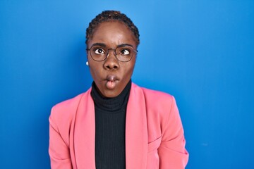 Fototapeta premium Beautiful black woman standing over blue background making fish face with lips, crazy and comical gesture. funny expression.