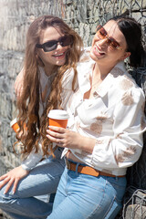Lifestyle concept.Two beautiful women having fun in city during sunny summer day. Models smiling, talking with each other and drinking coffee. Sun flare effect applied. Image contains motion blur