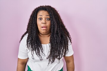 Plus size hispanic woman standing over pink background afraid and shocked with surprise and amazed...