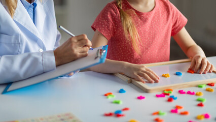 Little girl making words from colorful plastic letters during meeting with psychologist