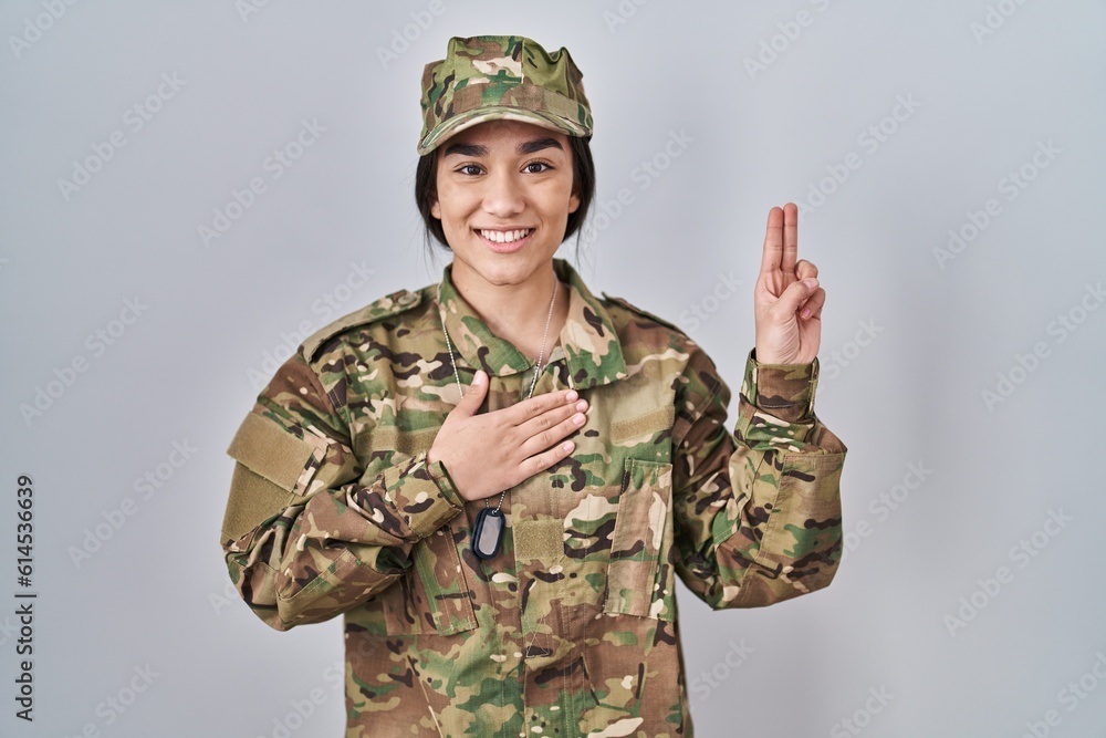 Canvas Prints Young south asian woman wearing camouflage army uniform smiling swearing with hand on chest and fingers up, making a loyalty promise oath