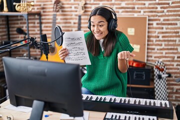 Fototapeta na wymiar Young south asian woman doing online music tutorial showing music sheet screaming proud, celebrating victory and success very excited with raised arm
