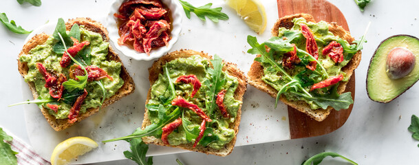 A narrow view of avocado and arugula toast topped with sun dried tomatoes.