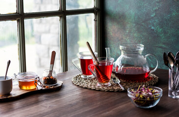 Hibiscus tea served with honey on a dark table near a window.