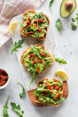 Top down view of avocado and arugula toast topped with sun dried tomatoes.