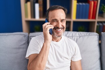 Middle age man talking on smartphone sitting on sofa at home