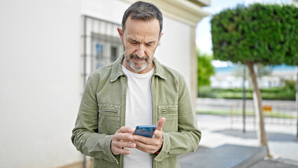 Middle age man using smartphone with serious expression at street