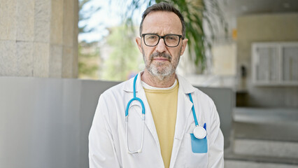 Middle age man doctor standing with serious expression at hospital
