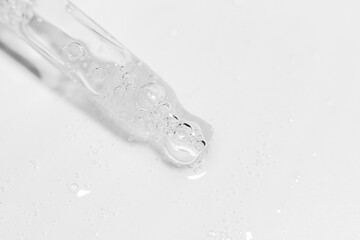 Transparent pipette with gel or liquid flowing out on a light background.