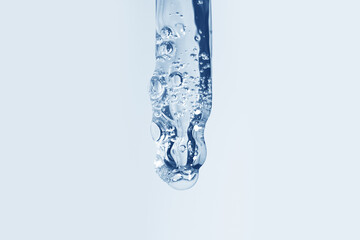 Transparent gel flowing from an eyedropper on a background with blue hues
