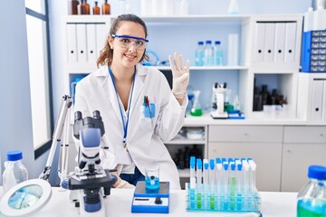 Fototapeta premium Young hispanic woman working at scientist laboratory showing and pointing up with fingers number four while smiling confident and happy.