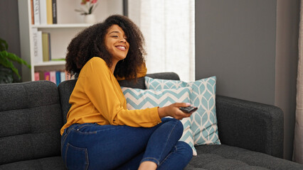 African american woman watching tv sitting on sofa at home