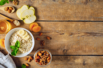 Dry raw oatmeal with ingredients for cooking healthy breakfast on wooden table with copy space top view